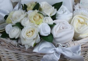 Basket of baby clothes rolled to look like flowers arranged in a bouquet